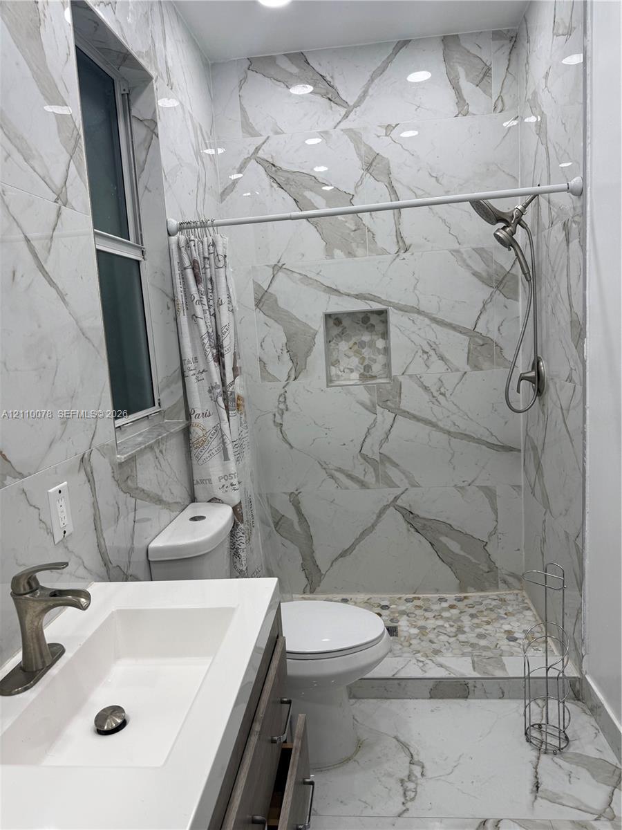 Full-height wall tiling with veined pattern, walk-in shower with pebble-tile flooring and recessed niche, floating vanity with integrated rectangular sink, and metallic finish faucet hardware