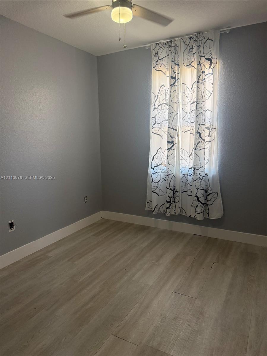 Room featuring wood-finish flooring, neutral-toned walls, and a ceiling-mounted fan with integrated lighting