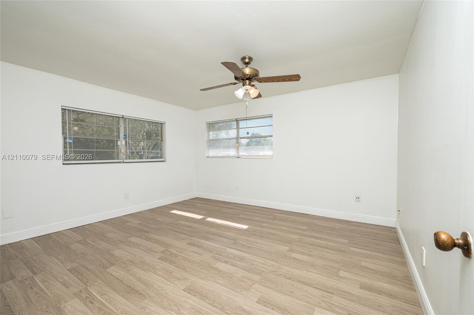 Interior space featuring wood-finish flooring, dual windows with horizontal blinds, and a central ceiling fan with an integrated light fixture Interior space featuring wood-finish flooring, dual windows with horizontal blinds, and a central ceiling fan with an integrated light fixture