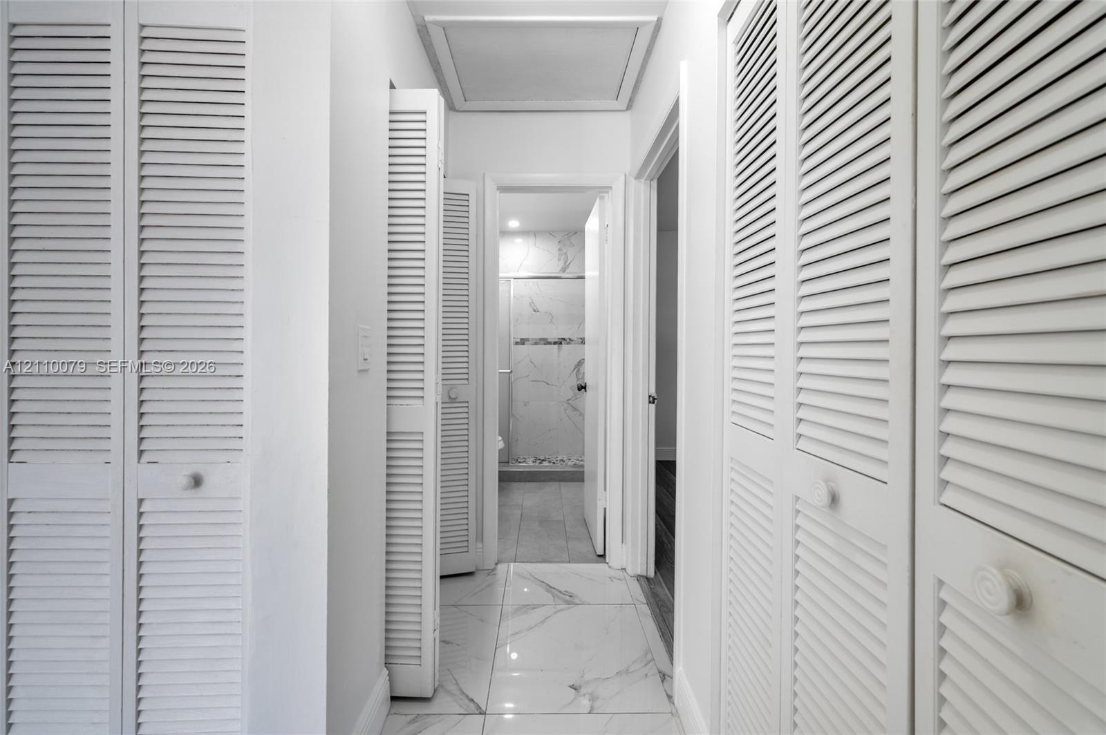 Hallway featuring large-format tile flooring with a neutral finish, multiple white louvered-style closet doors, and recessed ceiling lighting