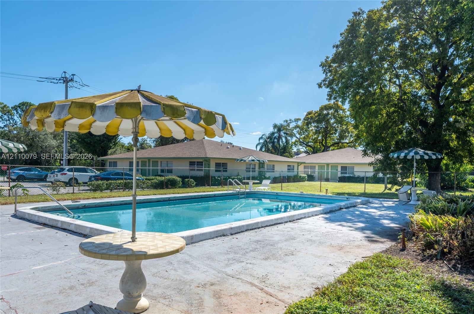In-ground swimming pool with a concrete deck, enclosed by perimeter fencing and surrounded by mature trees