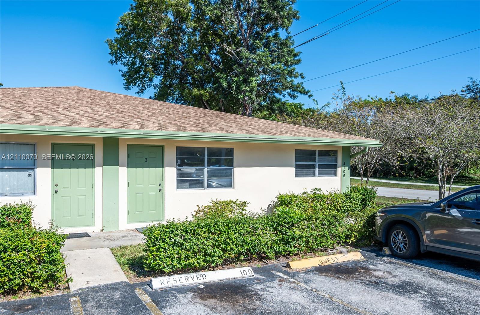 Single-story exterior featuring light-toned stucco, shingled roofing, dual entrance doors, and designated asphalt parking Single-story exterior featuring light-toned stucco, shingled roofing, dual entrance doors, and designated asphalt parking