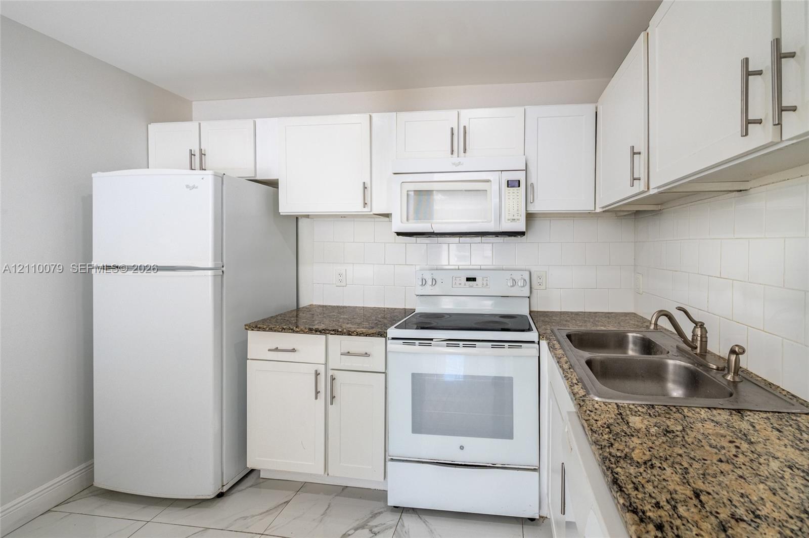 Kitchen featuring white cabinetry, stone-finish countertops, subway tile backsplash, white appliances, and a dual-basin stainless steel sink Kitchen featuring white cabinetry, stone-finish countertops, subway tile backsplash, white appliances, and a dual-basin stainless steel sink