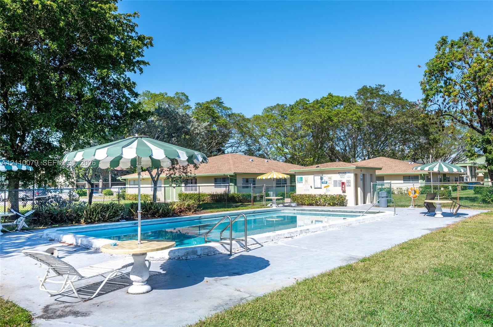 Outdoor swimming pool featuring a concrete deck and metal perimeter fencing, surrounded by mature trees