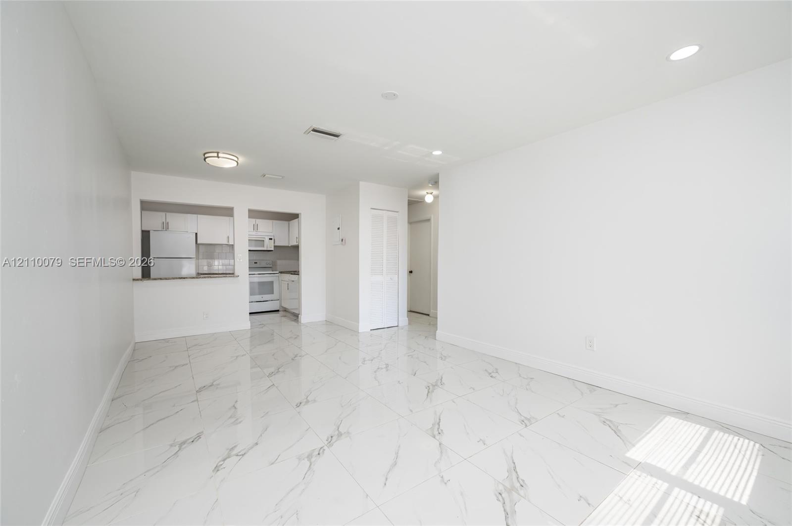Large-format tile flooring with veining, white cabinetry, integrated pass-through, recessed lighting, and flush-mount ceiling fixture Large-format tile flooring with veining, white cabinetry, integrated pass-through, recessed lighting, and flush-mount ceiling fixture