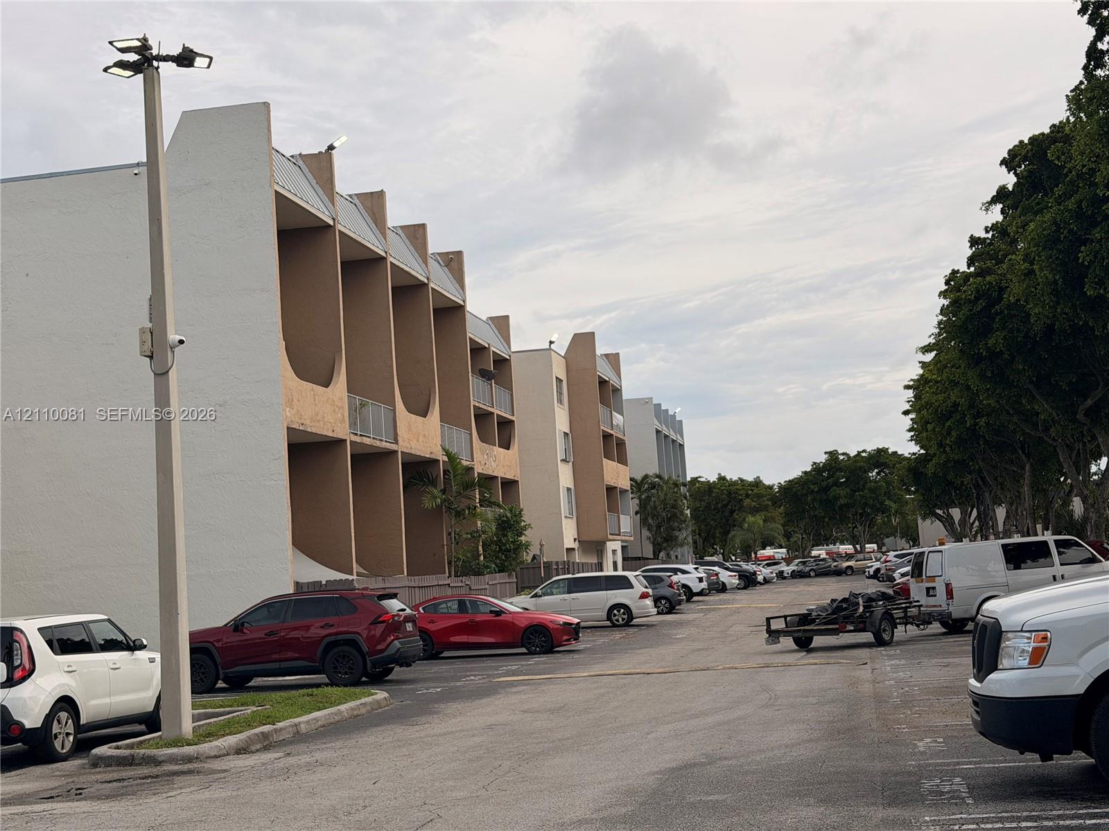 Multi-story building exterior featuring vertical concrete structural fins, recessed balconies, and paved surface parking
