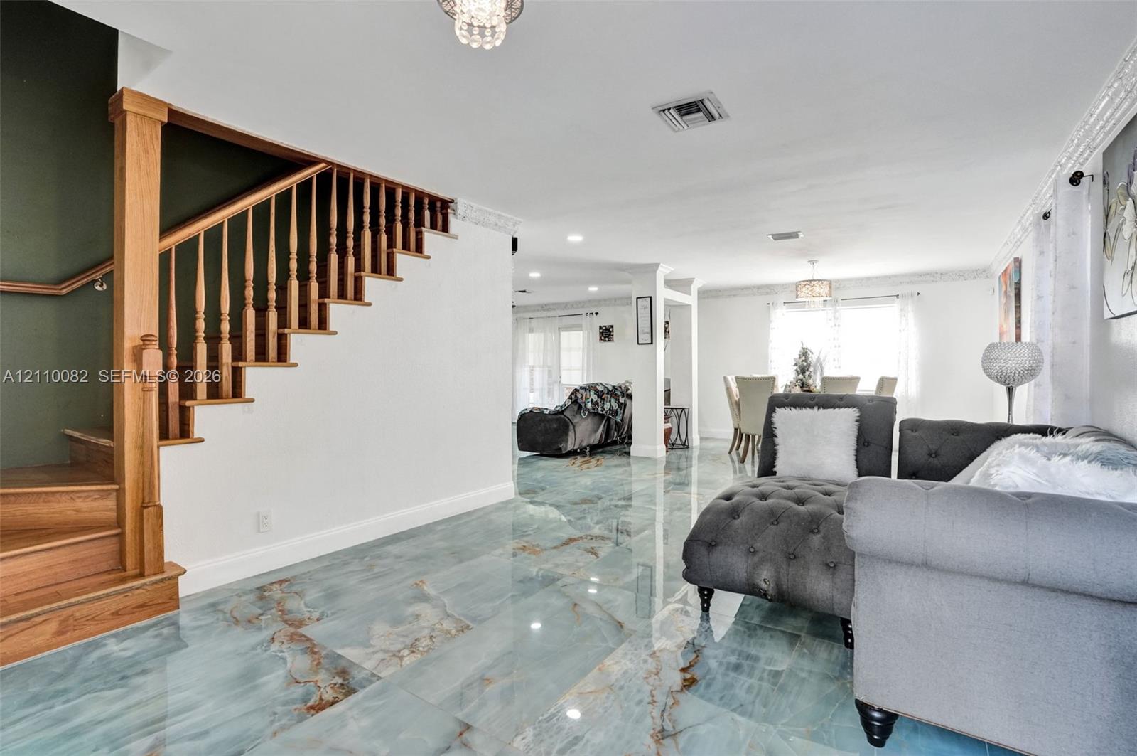 Polished large-format stone flooring featuring prominent blue and copper veining, complemented by a solid wood staircase with custom balusters, integrated recessed lighting, and ornate crown molding