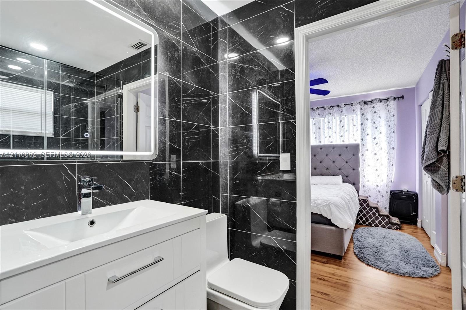 Bathroom featuring black stone-tile wall cladding, a white vanity with integrated basin, polished chrome faucet, and a wall-mounted LED-backlit mirror