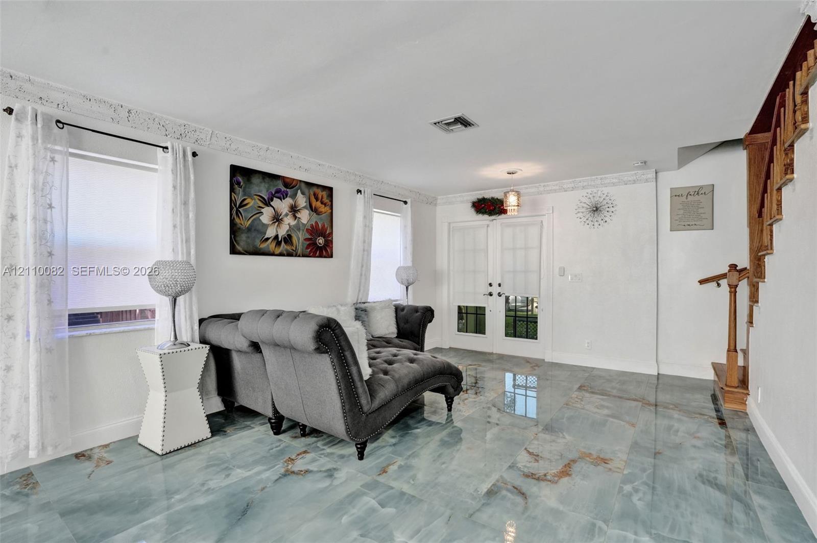 Polished stone flooring with natural veining, double-entry doors with glass paneling, decorative crown molding, and a wooden staircase featuring a stained handrail
