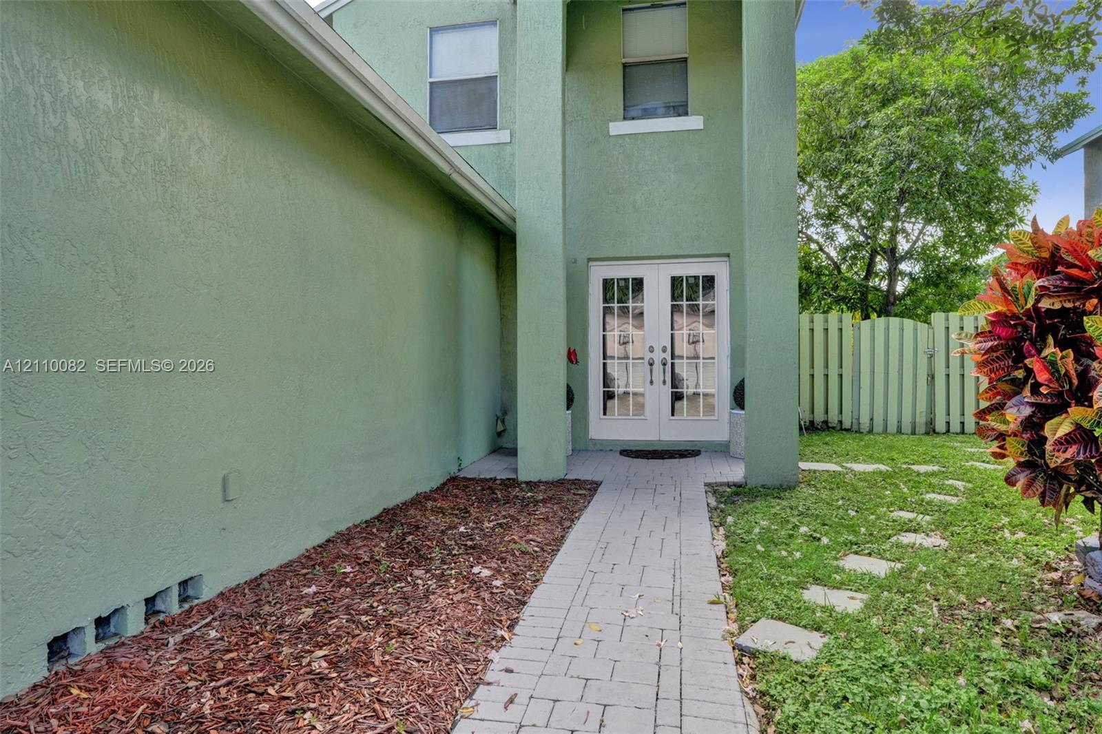 Stucco exterior featuring double glass-paneled entry doors, a paved walkway, and a privacy fence