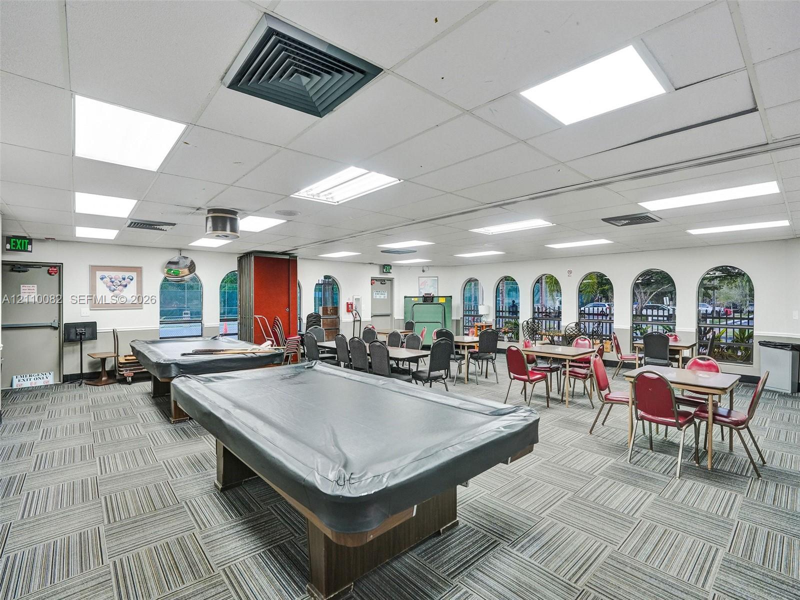 Large multipurpose room featuring a drop ceiling with integrated rectangular lighting, carpet tile flooring, and multiple arched windows
