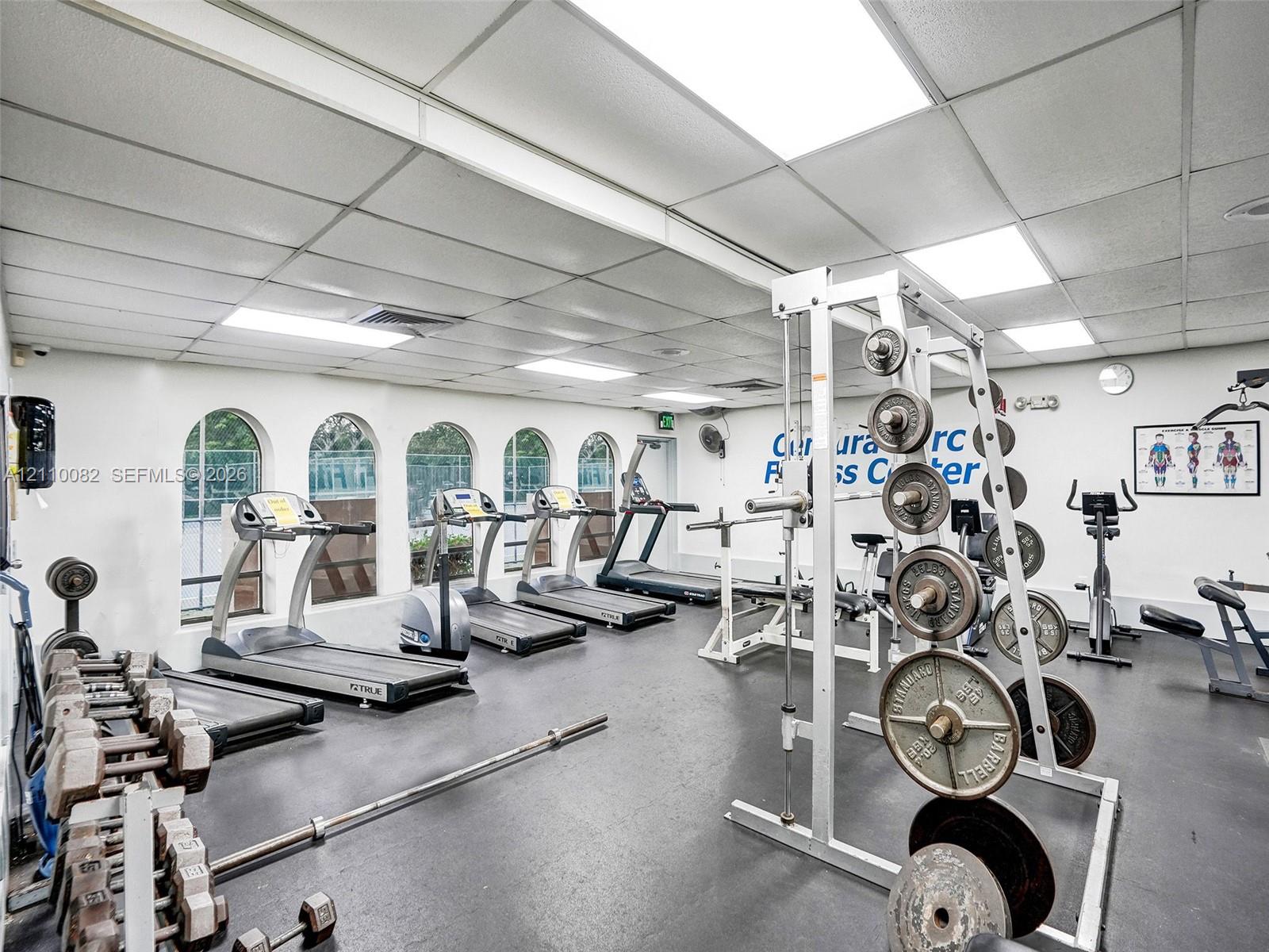 Fitness center featuring recessed lighting, a grid ceiling system, durable rubberized flooring, and multiple arched windows