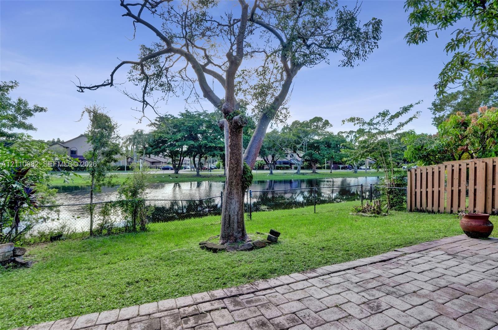 Rear yard featuring a paver patio, lawn, mature tree, chain-link fencing, and water frontage