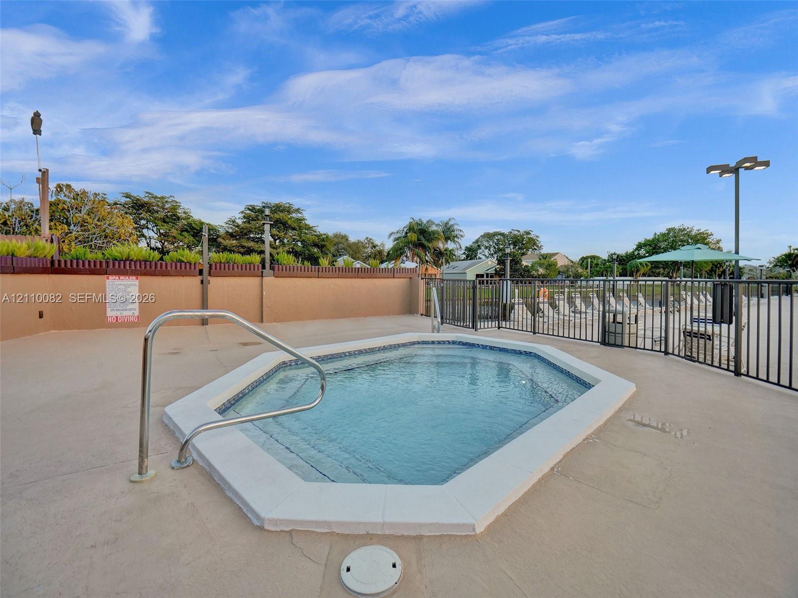In-ground spa with tile detailing, concrete deck, and metal perimeter fencing
