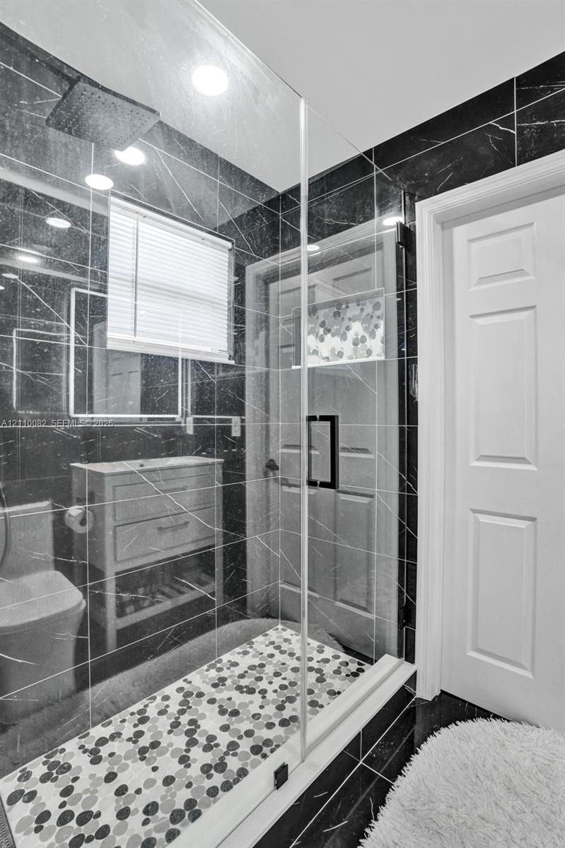 Walk-in shower enclosure featuring dark veined wall tile, a multi-textured stone-patterned floor, a built-in recessed wall niche, and a contemporary rain-style showerhead