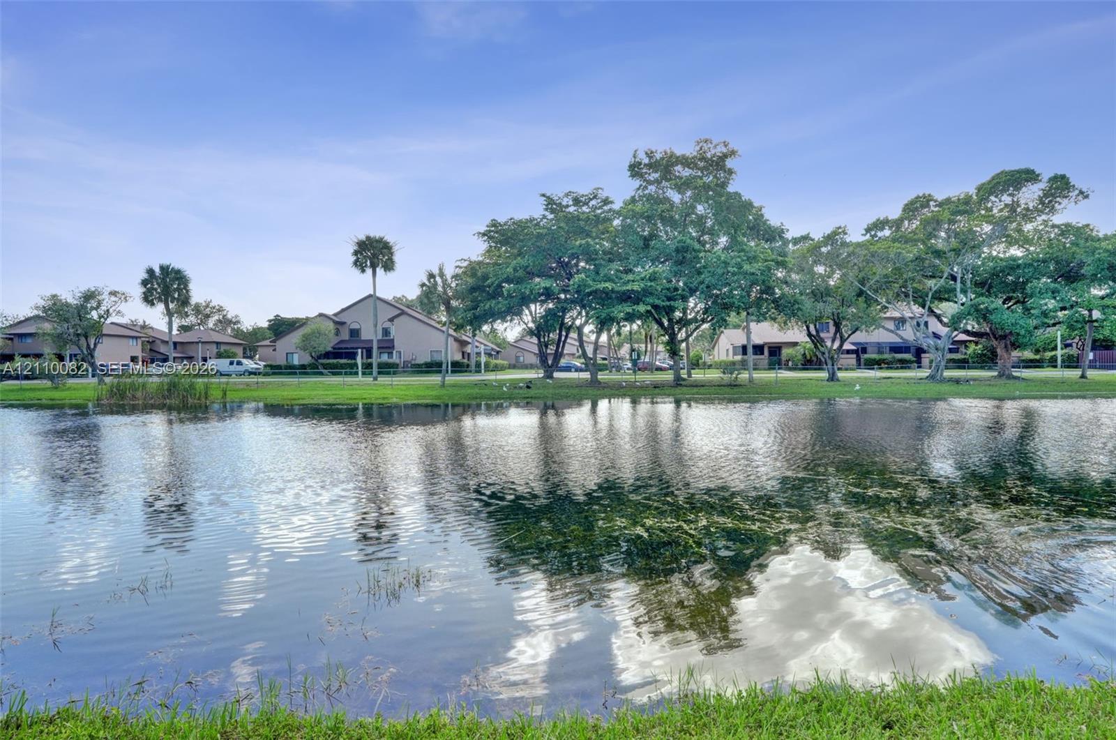 Waterfront setting featuring a pond, mature shade trees, and manicured green space