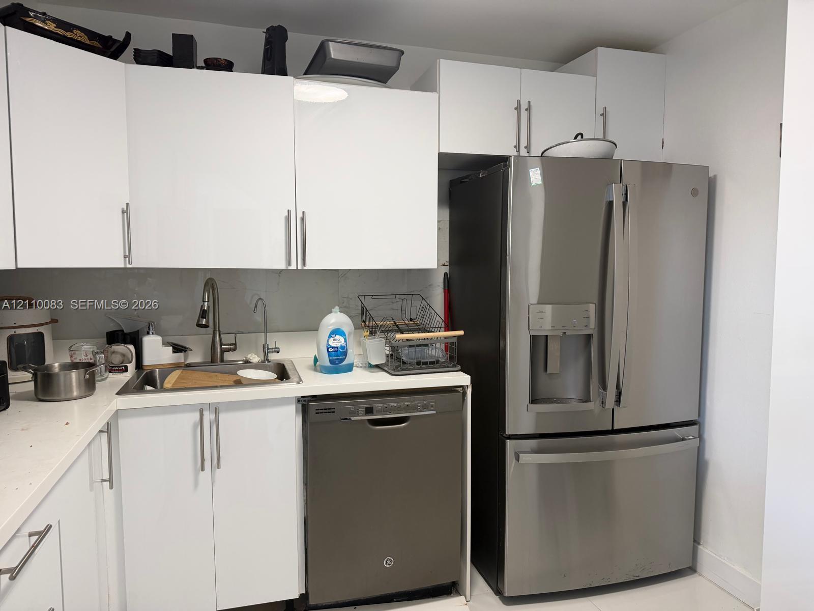 Modern kitchen area featuring flat-panel white cabinetry, white countertops, stainless steel French-door refrigerator, integrated stainless steel dishwasher, and a single-basin undermount sink with a high-arch pull-down faucet Modern kitchen area featuring flat-panel white cabinetry, white countertops, stainless steel French-door refrigerator, integrated stainless steel dishwasher, and a single-basin undermount sink with a high-arch pull-down faucet