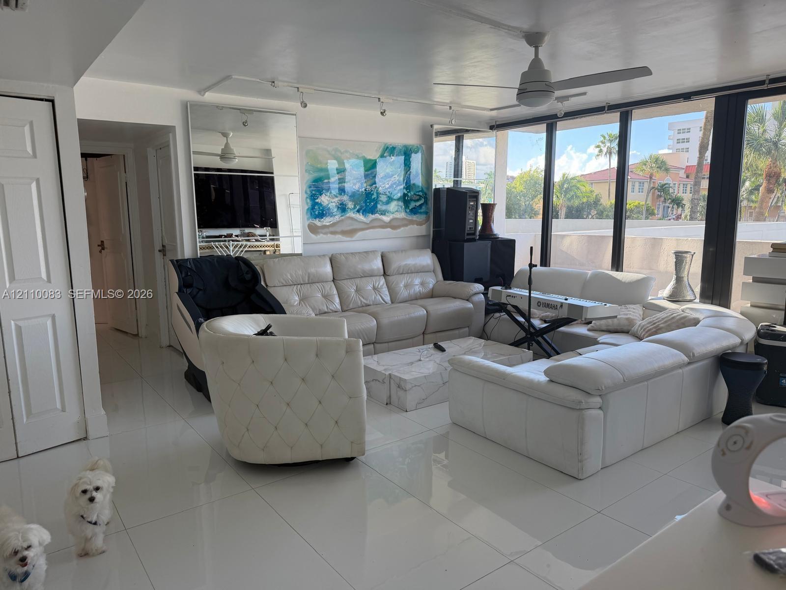 Living area featuring large-format tile flooring, floor-to-ceiling windows, full-length wall mirror, ceiling fan, and adjustable track lighting Living area featuring large-format tile flooring, floor-to-ceiling windows, full-length wall mirror, ceiling fan, and adjustable track lighting