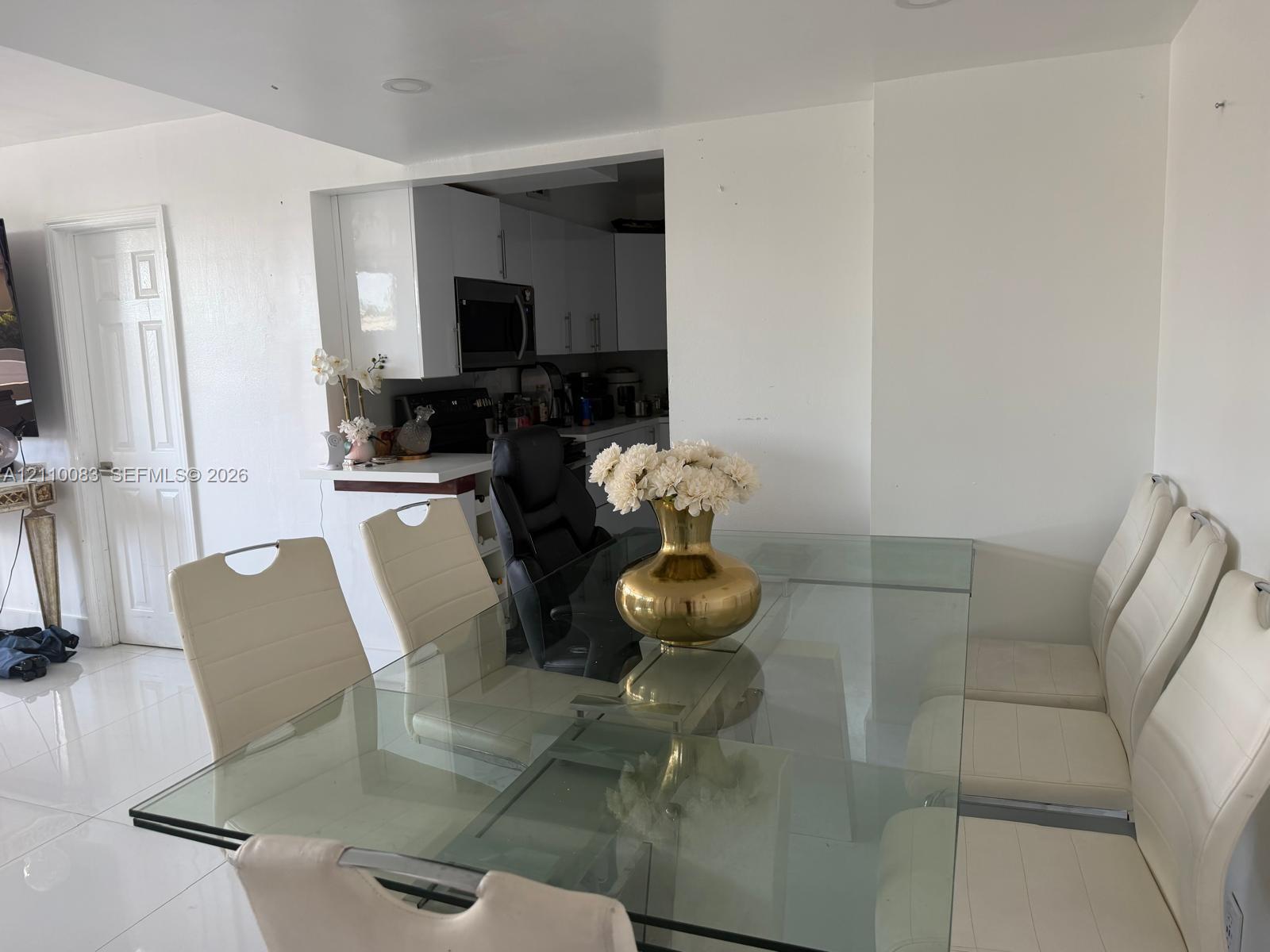 Dining area featuring high-gloss tile flooring, recessed ceiling lighting, and a neutral color palette, opening to a kitchen equipped with white cabinetry and a built-in microwave Dining area featuring high-gloss tile flooring, recessed ceiling lighting, and a neutral color palette, opening to a kitchen equipped with white cabinetry and a built-in microwave