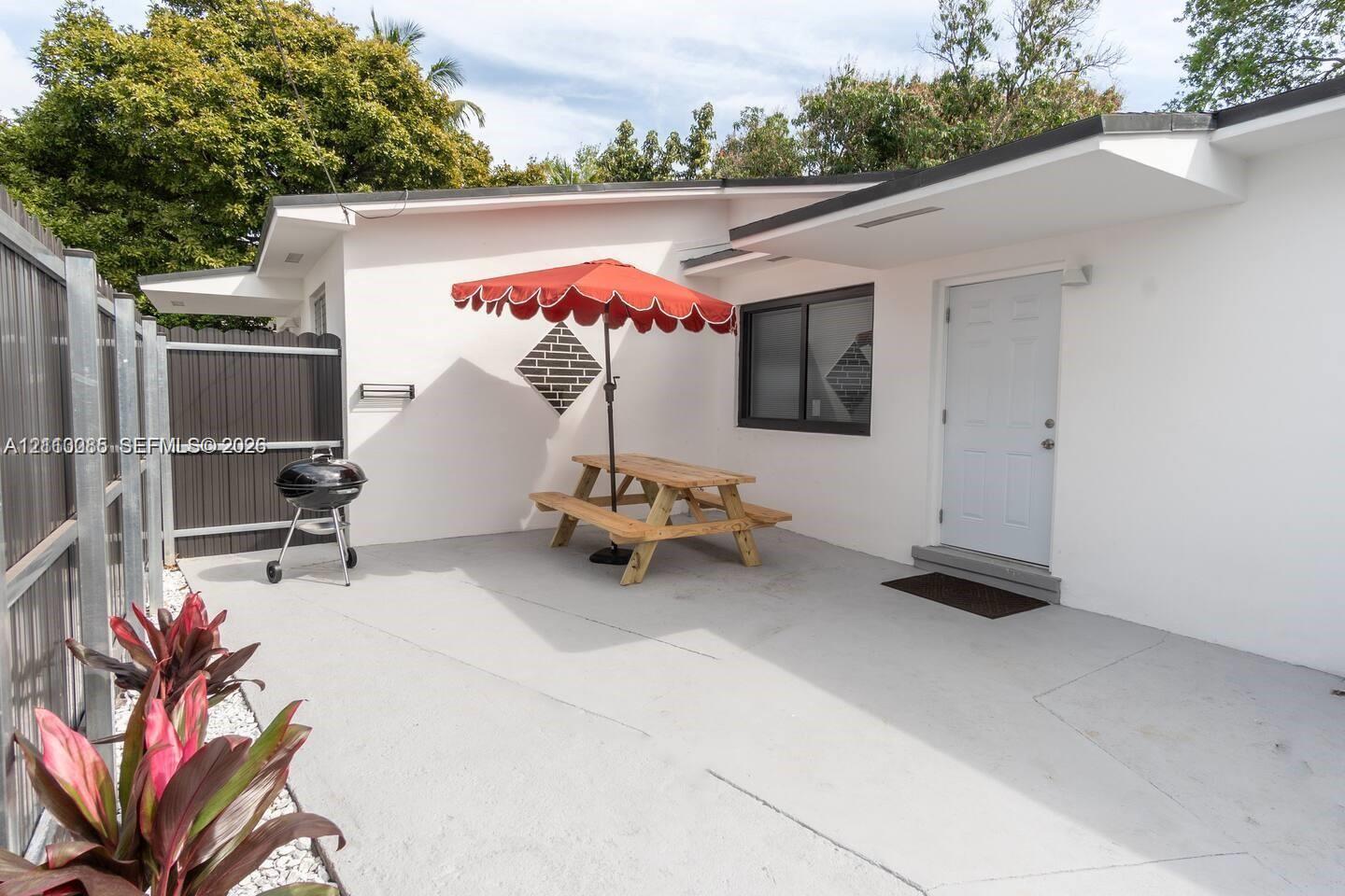 Concrete patio featuring a vertical wood-slat privacy fence, exterior white stucco siding, and dark-trimmed window frames