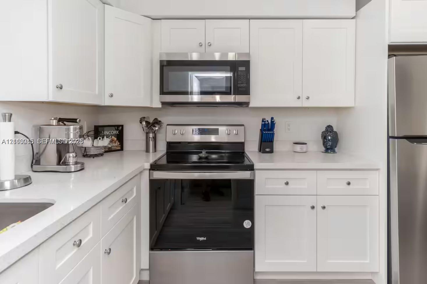 Kitchen featuring white shaker-style cabinetry, solid-surface countertops, and a full suite of stainless steel appliances, including an over-the-range microwave and a smooth-top range