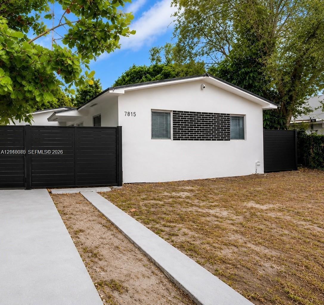 Exterior featuring white stucco siding, contrasting black brick masonry accents, dark horizontal privacy fencing, and a concrete driveway