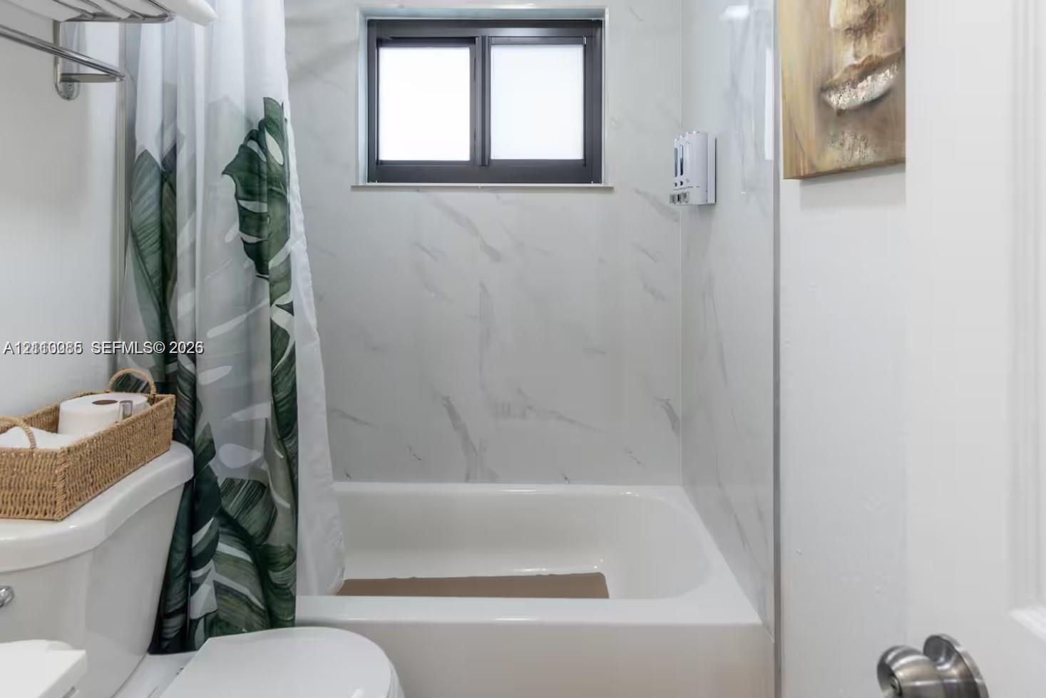 Full-height shower surround featuring large-format stone-pattern tile, white porcelain soaking tub, horizontal sliding window, and chrome wall-mounted towel rack
