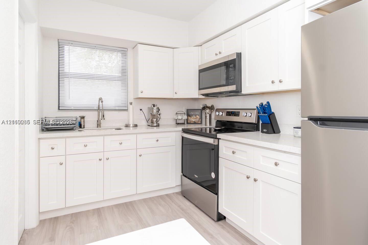 Kitchen featuring white Shaker-style cabinetry, solid-surface countertops, wood-finish flooring, and stainless steel appliances including a built-in microwave and range