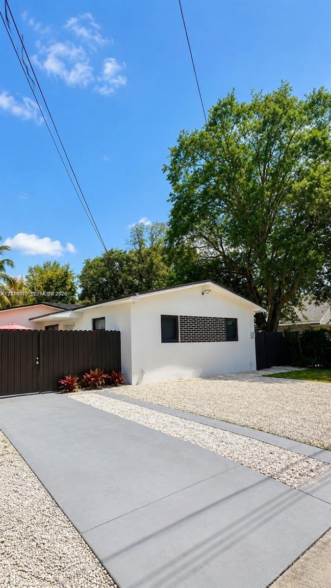Exterior featuring white stucco siding, a concrete ribbon driveway, decorative privacy fencing, and a gravel front courtyard