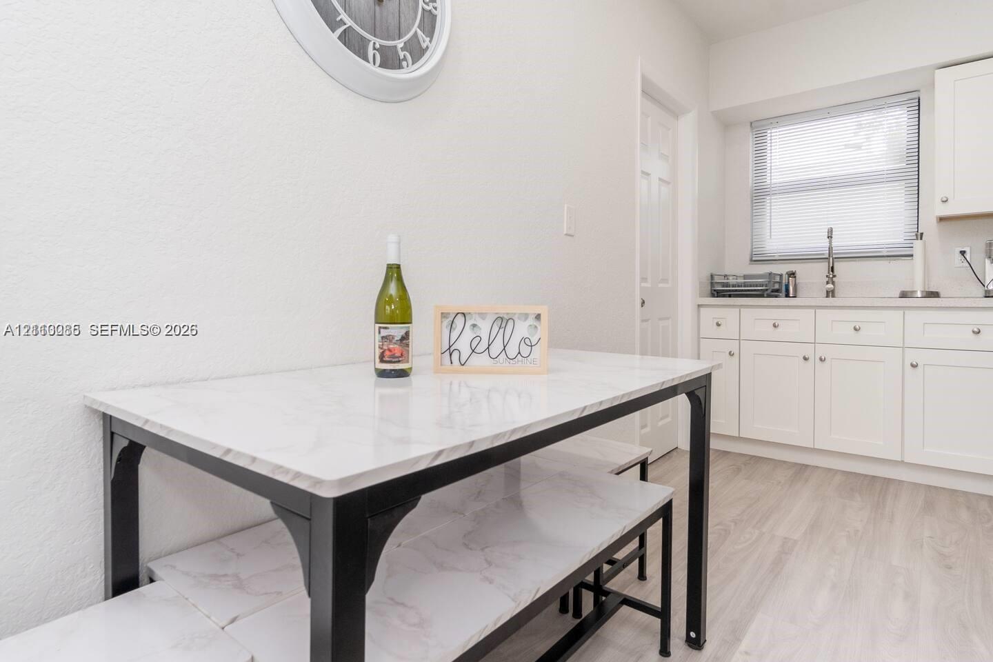 White Shaker-style cabinetry, solid-surface countertops, stainless steel faucet, and light-toned wood-finish flooring