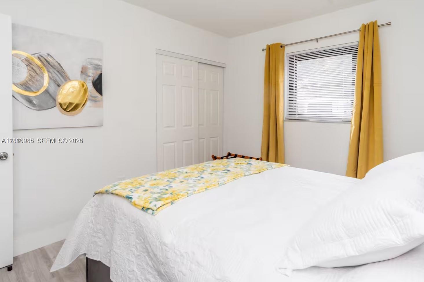 Bedroom featuring light-toned wood-finish flooring, a double-panel sliding closet door, and a horizontal window with adjustable metal blinds