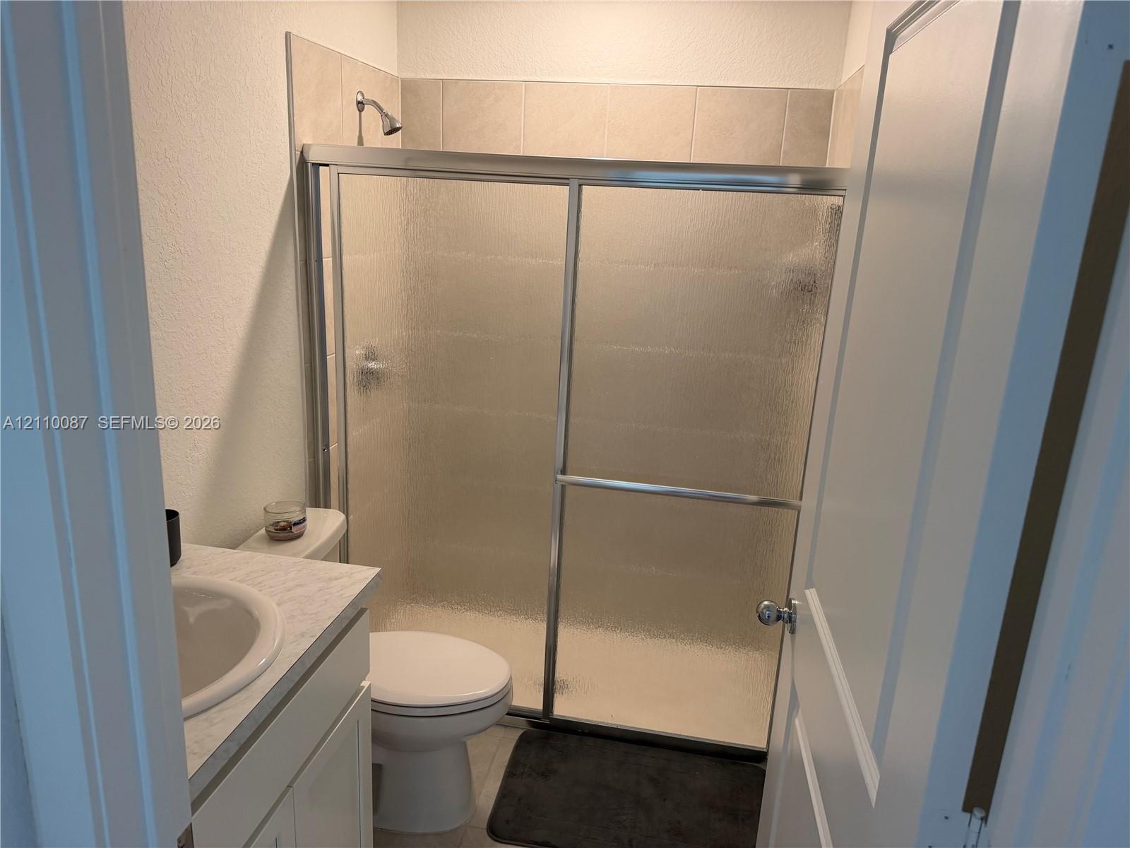 Bathroom featuring a vanity with a stone-finish countertop and integrated sink, a walk-in shower with a sliding glass door, and neutral tile wall surround