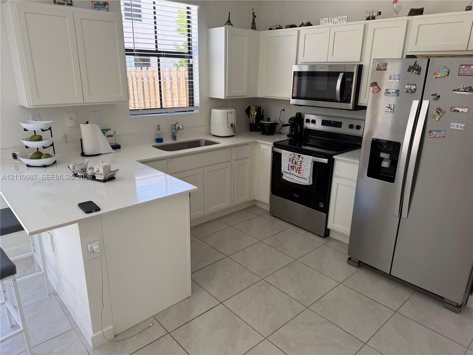 Kitchen featuring white shaker-style cabinetry, white countertops with an integrated breakfast bar, stainless steel appliances, and tile flooring