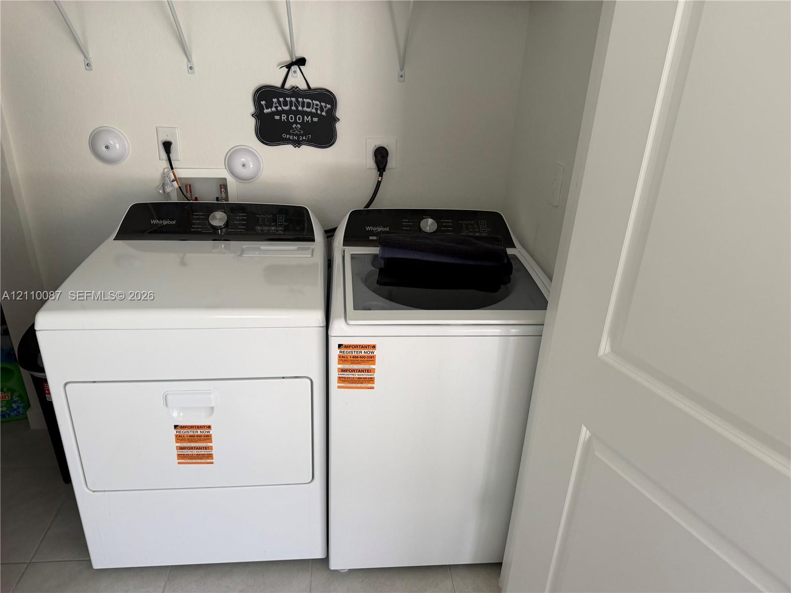 Utility area featuring side-by-side white clothes washer and dryer units, integrated utility hookups, and overhead wall-mounted shelving