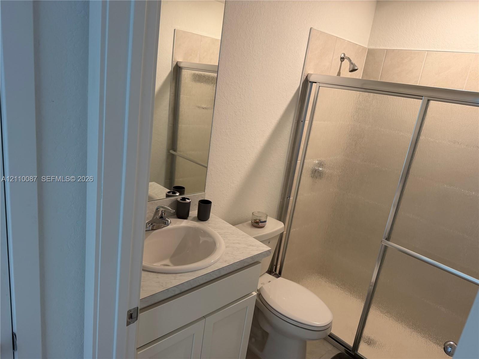 Bathroom featuring a single-sink vanity with a stone-composite countertop, chrome faucet hardware, and a shower enclosure with sliding textured glass doors and tile surround