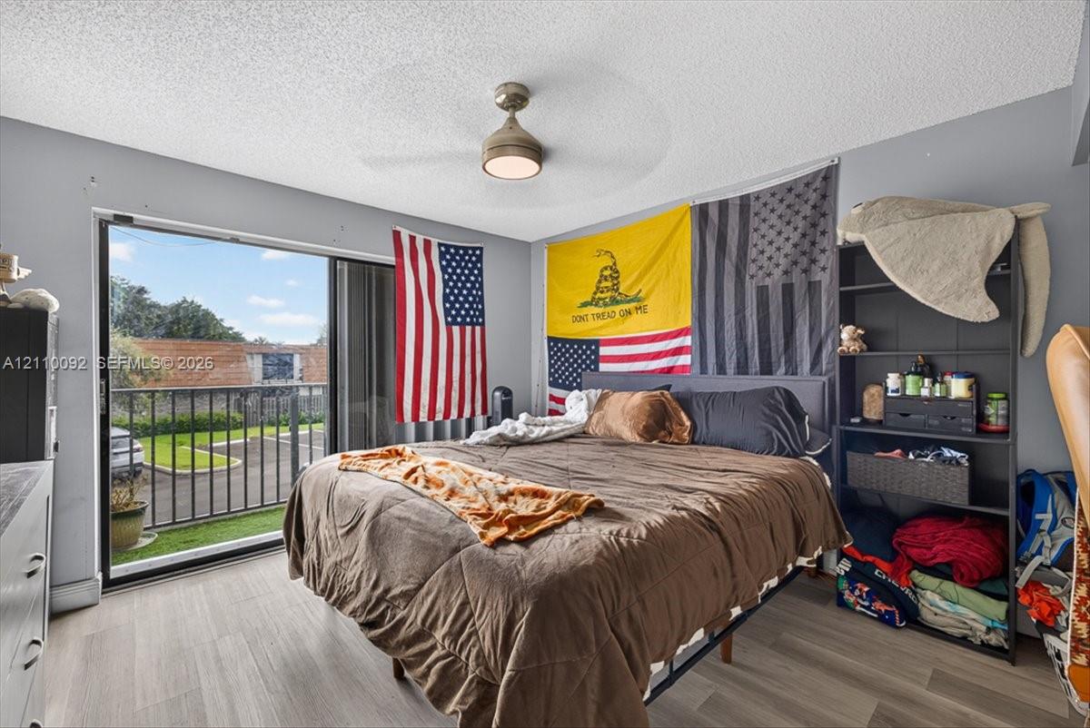 Sliding glass door leading to a private balcony with metal railing, wood-finish flooring, and a ceiling-mounted light fixture with integrated fan