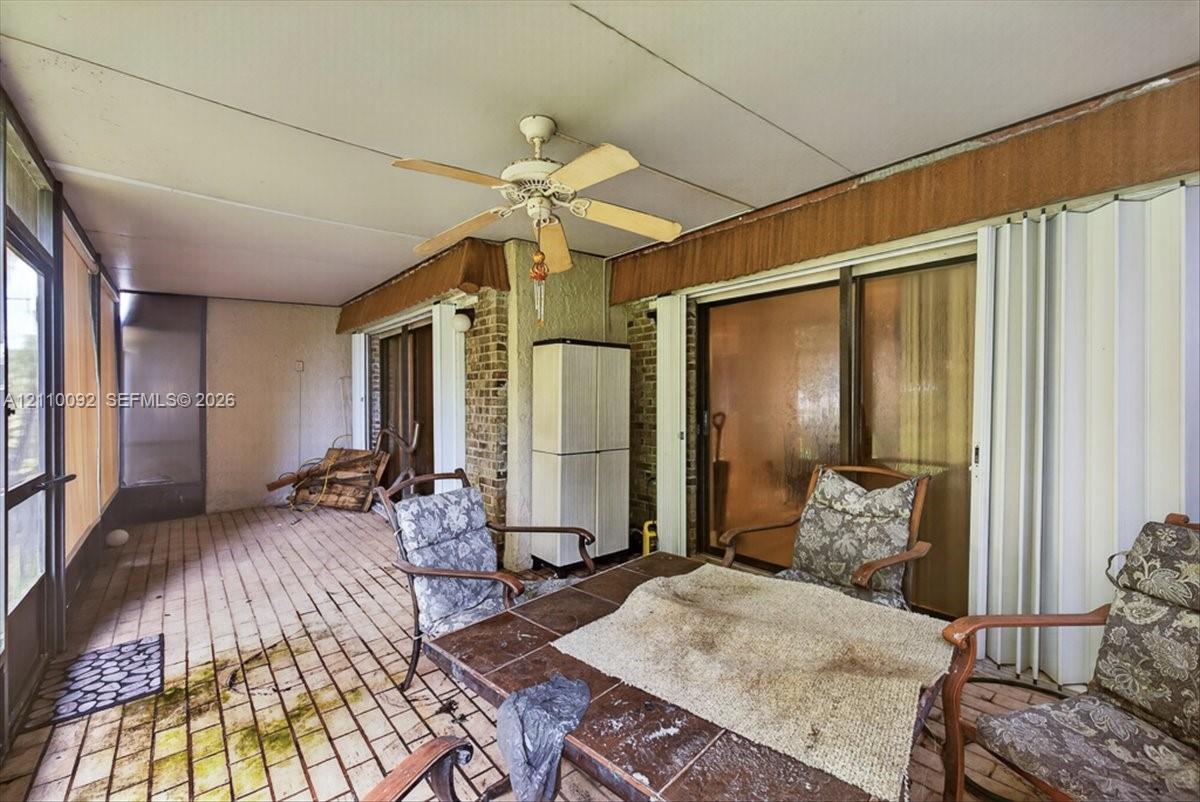 Enclosed sunroom featuring brick flooring, brick exterior wall accents, a ceiling fan, and sliding glass door access