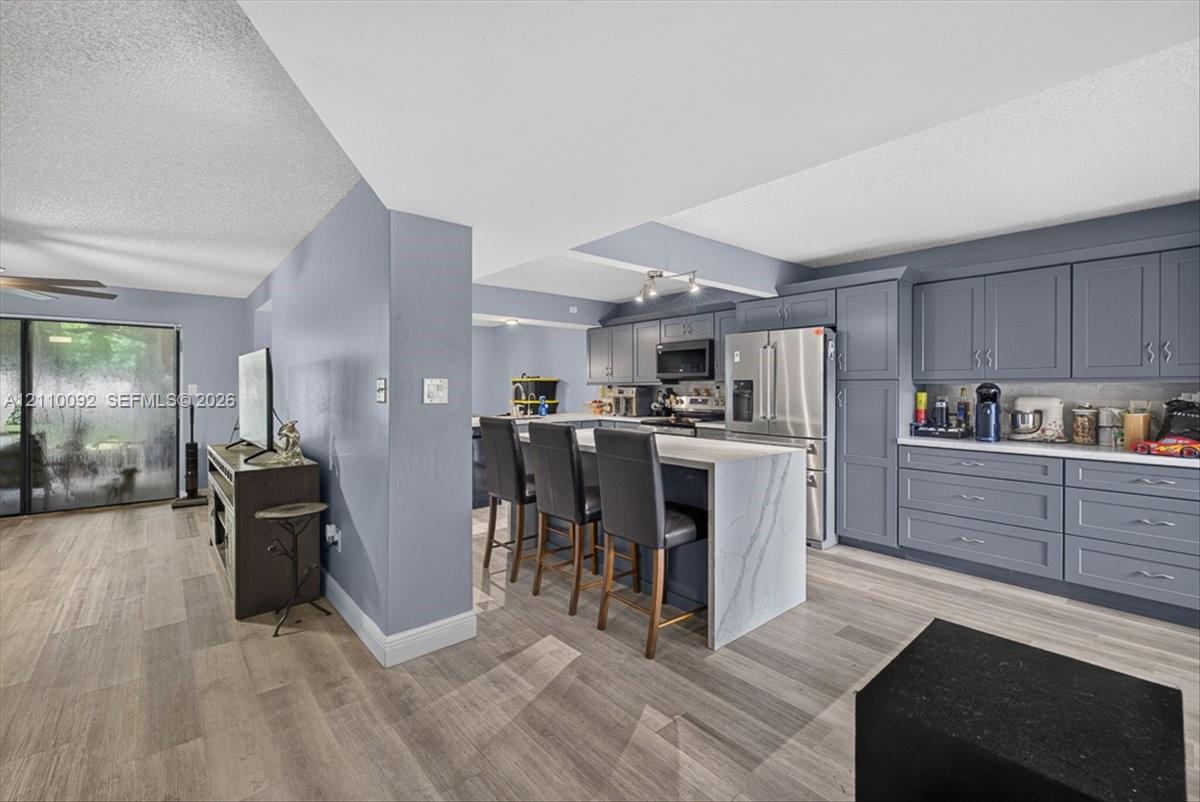 Kitchen featuring gray shaker-style cabinetry, white waterfall-edge stone island, stainless steel appliances, and wood-finish flooring