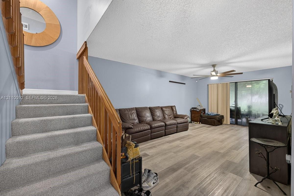 Staircase with wood-finish railings and carpeted treads, wood-finish flooring, ceiling fan with integrated lighting, and sliding glass doors