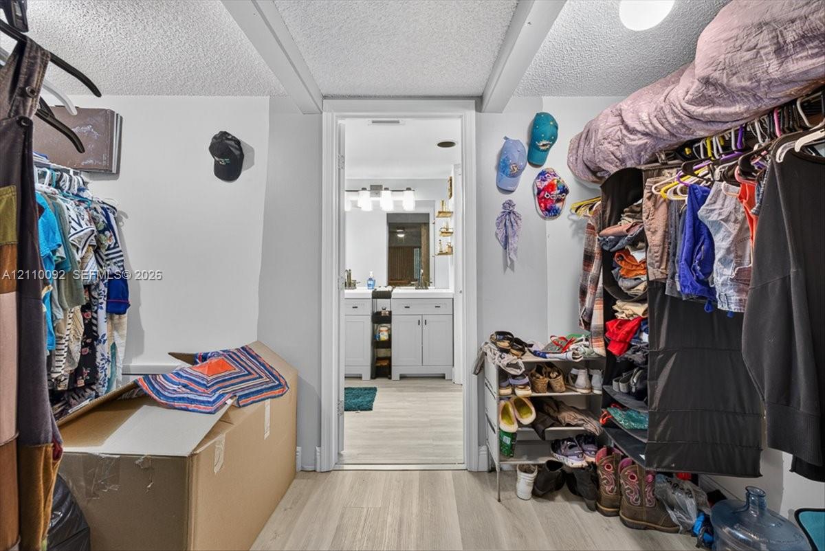 Walk-in closet featuring tiered clothing rods and integrated upper shelving, with light-toned wood-finish flooring