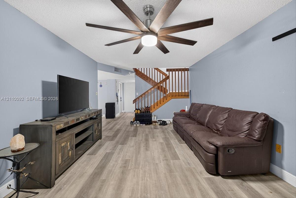Wood-finish flooring, multi-blade ceiling fan with integrated lighting, and wooden staircase featuring a slatted banister
