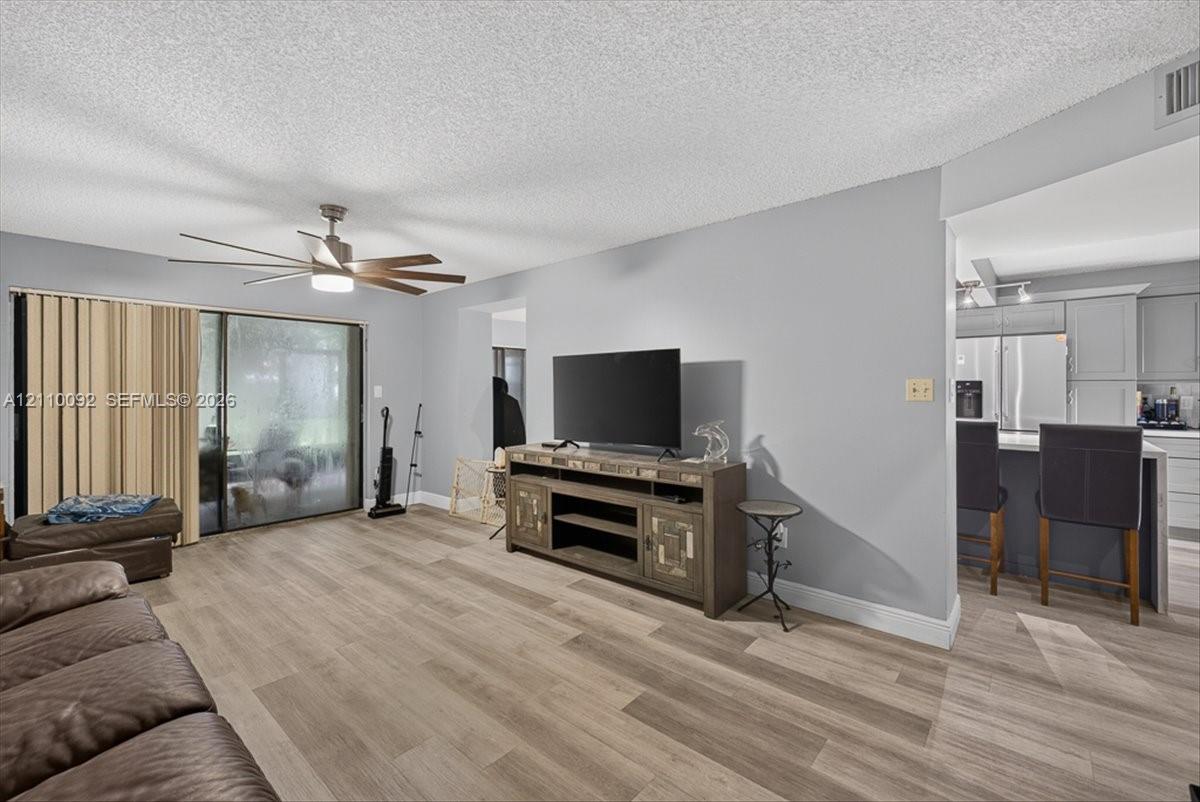 Living space featuring wood-finish flooring, a multi-blade ceiling fan, and large glass sliding doors
