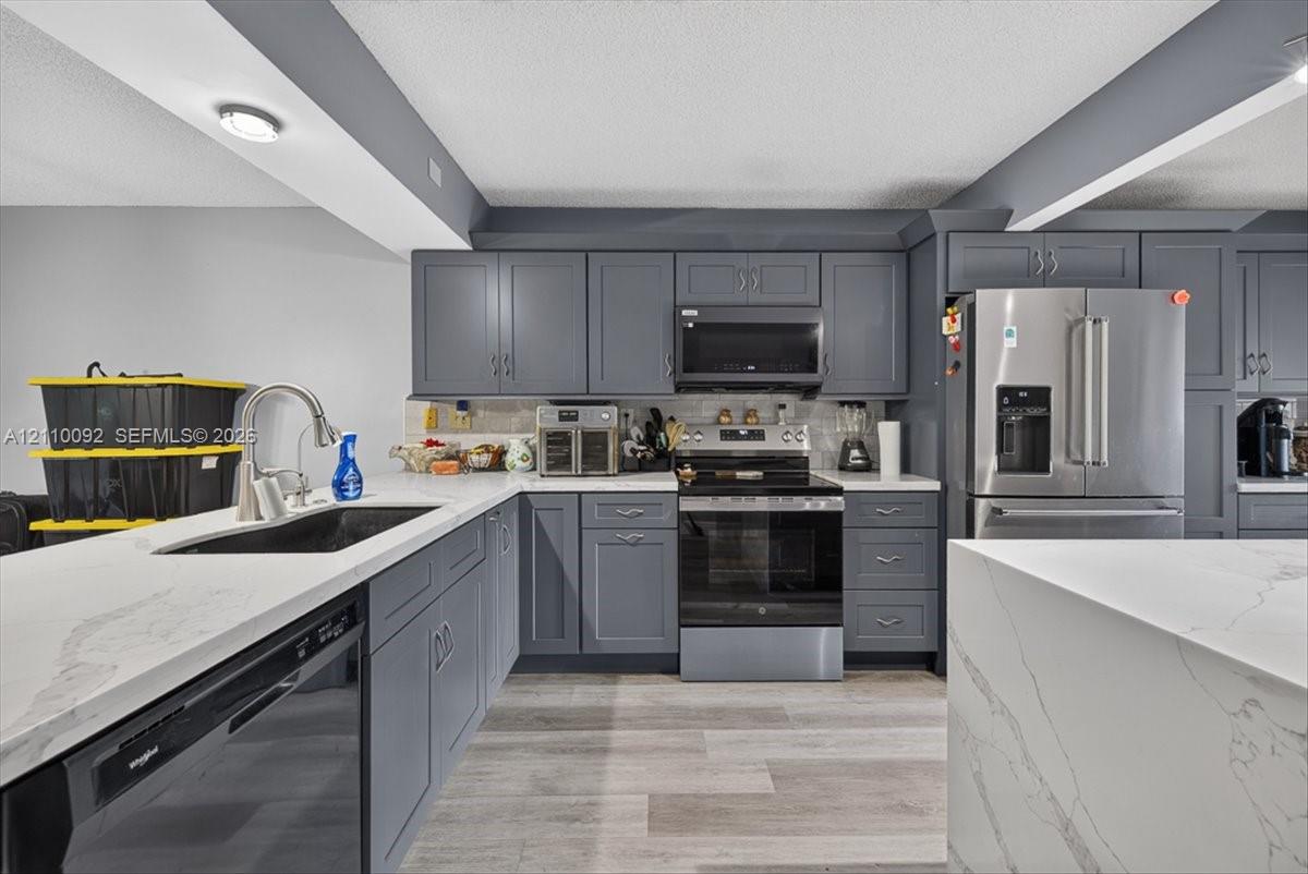 Kitchen featuring charcoal-toned shaker cabinetry, quartz countertops with veining, stainless steel appliances, and wood-finish flooring