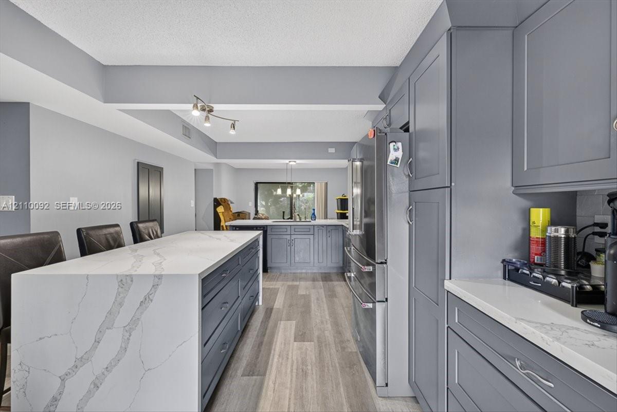 Kitchen featuring gray cabinetry, waterfall-edge quartz countertops, stainless steel appliances, and wood-finish flooring