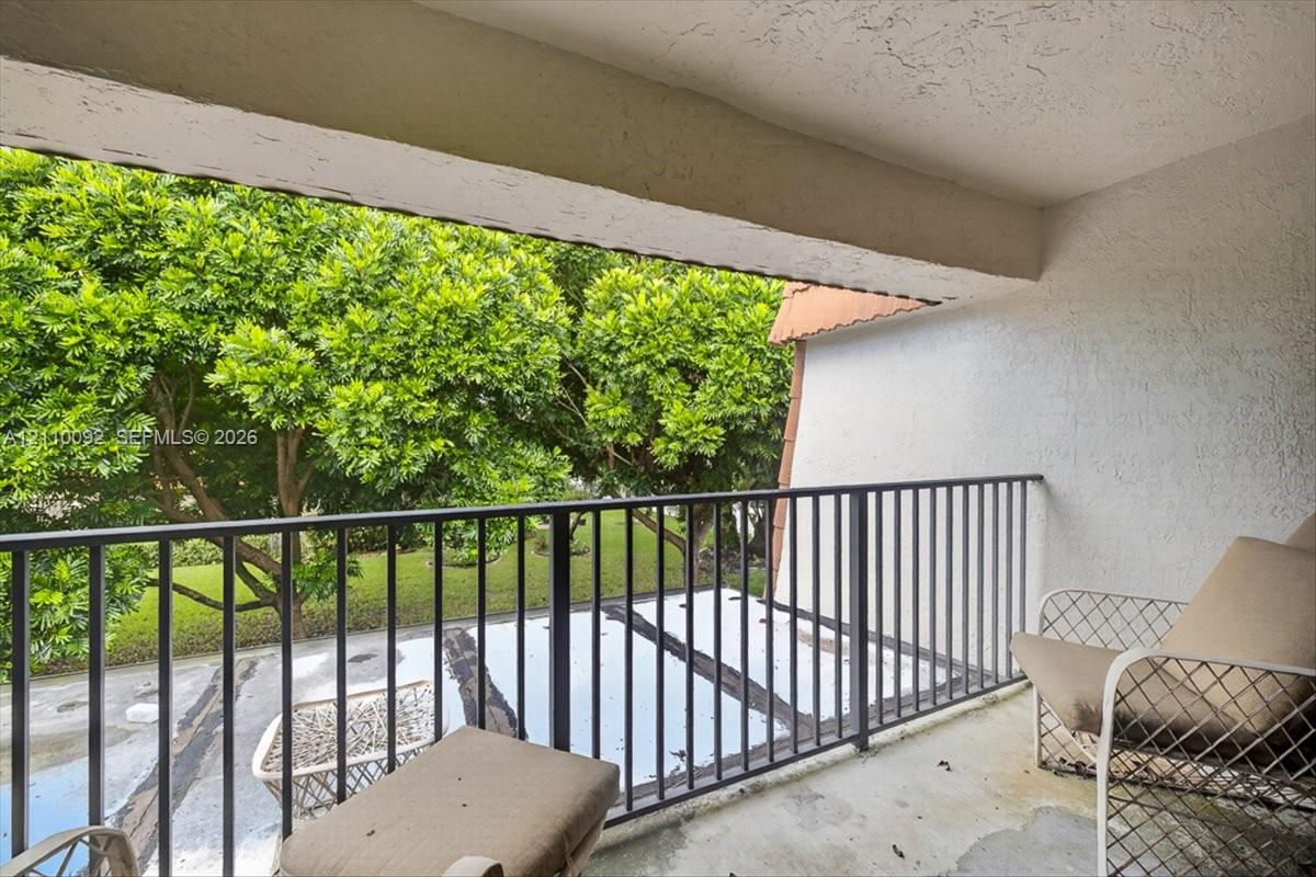 Covered balcony featuring concrete flooring, textured walls, and a black metal railing