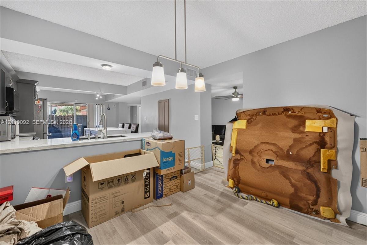 Kitchen featuring a pass-through counter, stone-finish countertops, stainless steel undermount sink, three-light linear pendant fixture, and wood-finish flooring