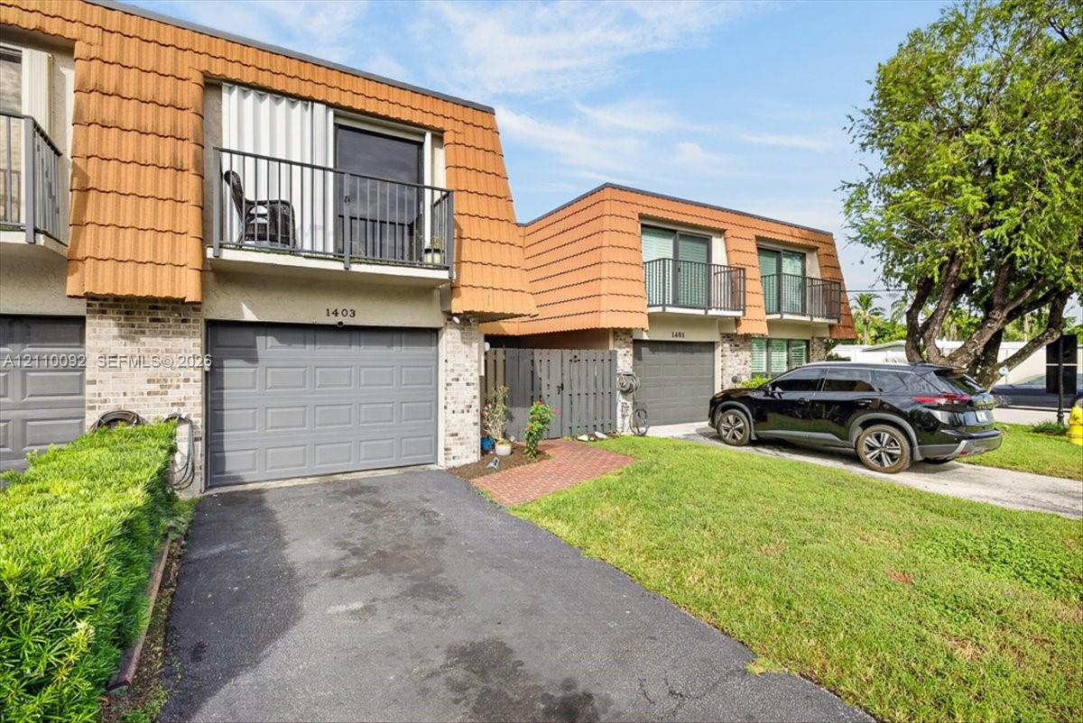 Multi-level exterior featuring terra cotta tile mansard roofing, brick veneer siding, private upper-level balconies with metal railings, and attached single-car garages