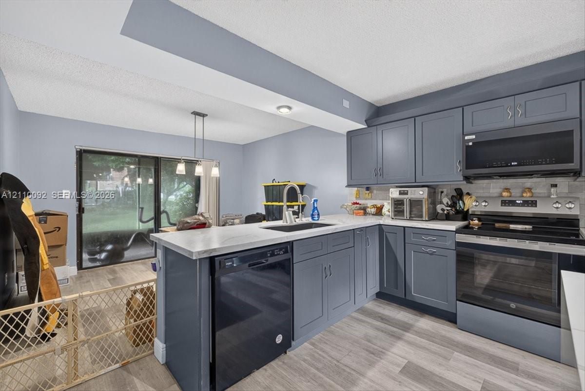 Kitchen featuring charcoal-toned cabinetry, light-toned countertop, undermount sink, stainless steel appliance suite, and wood-finish flooring