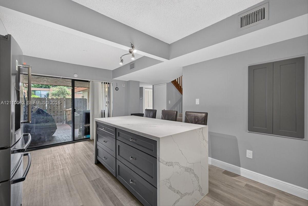 Kitchen island featuring dark cabinetry, a waterfall-edge countertop with integrated drawers, wood-finish flooring, and sliding glass doors