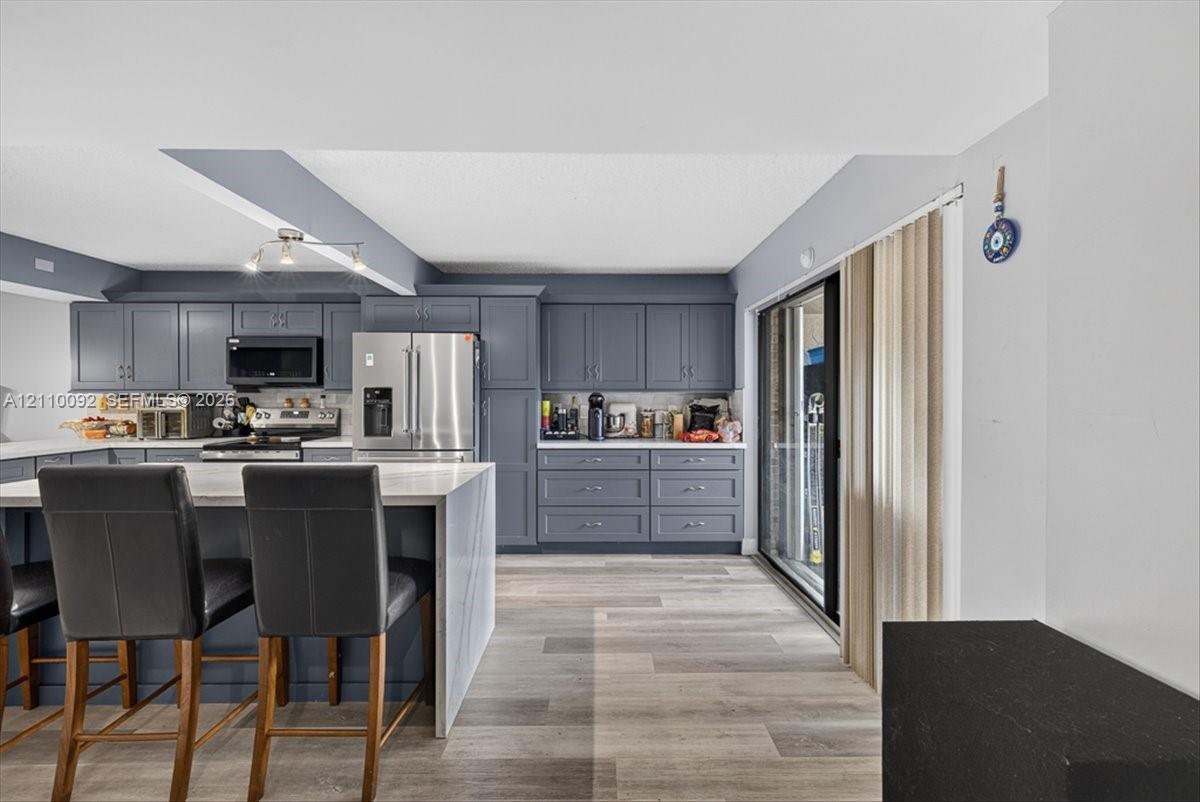 Kitchen featuring slate-grey shaker cabinetry, quartz countertops, a central island with bar seating, stainless steel appliances, and wood-finish flooring